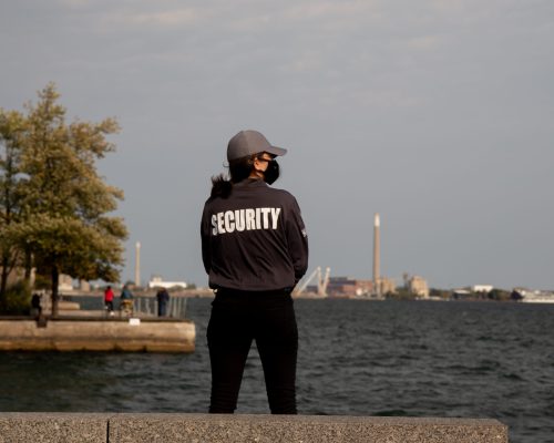 A closeup shot of a female security guard in uniform and mask watching over the harbor area