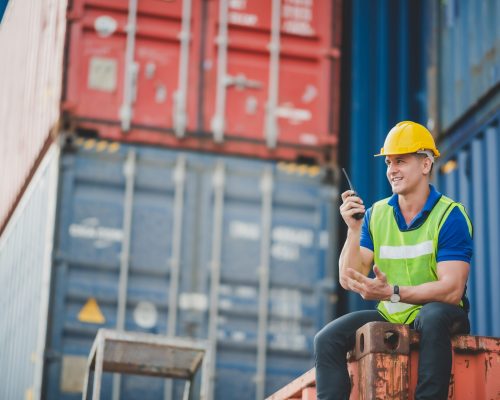 foreman worker manager working outdoor site, cargo container site, control plan working, working with safety equiments, helmet safety vest, technology walkie talkie concept.pointing finger