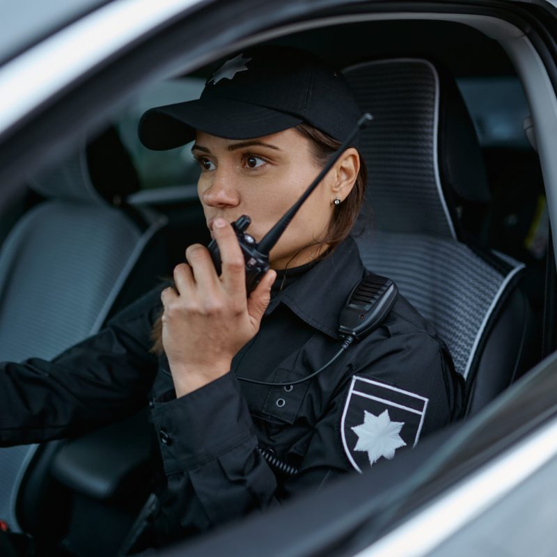 Woman police officer using walkie-talkie portable radio driving in car. Female cop patrolling street