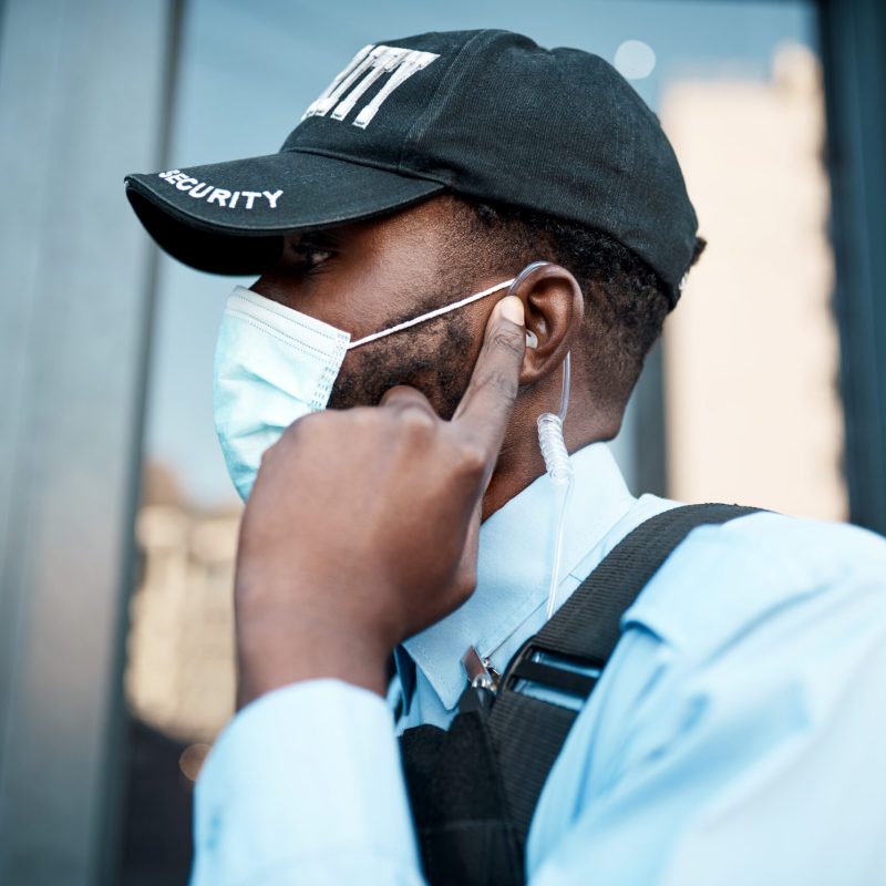 Shot of a masked young security guard using an earpiece while on patrol outdoors.